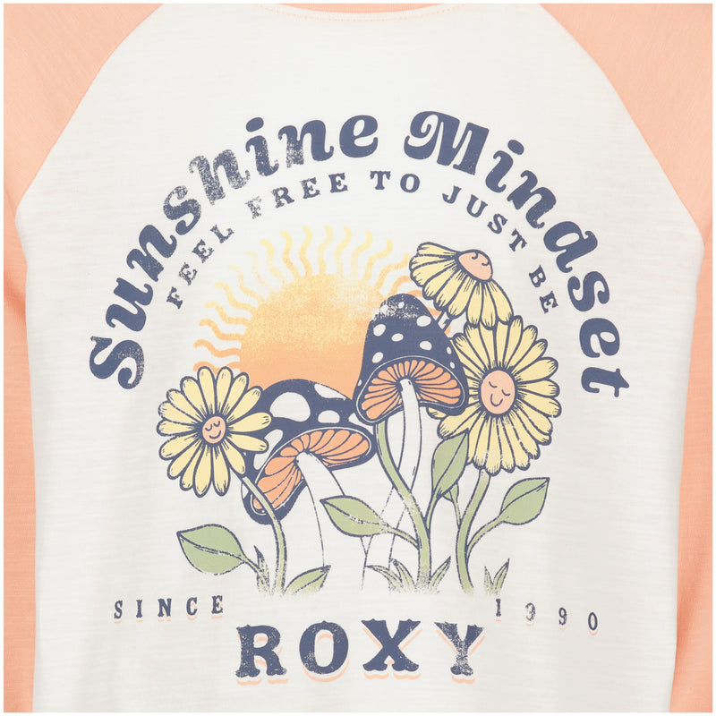 The Girls’ Sunshine Mindset Long Sleeve Tee by Roxy features a relaxed fit raglan style, adorned with a shirt design showcasing smiling mushrooms and flowers, a sun in the background, and text that reads “Sunshine Mindset, feel free to just be, since 1990, ROXY.”.