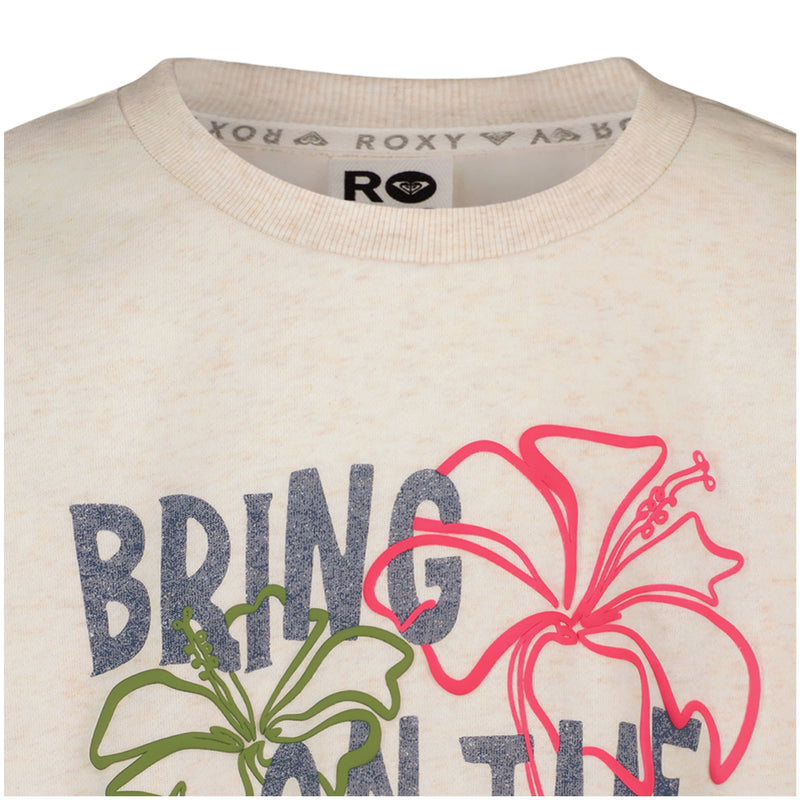 Close-up of a Roxy Girls' Sunshine Crew shirt collar in beige, featuring “BRING ON THE” in bold letters and two hibiscus flower prints—one green, one pink—on the chest.
