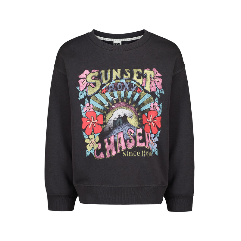 The Girls' Sunny Crew by Roxy is a black oversized sweatshirt with a vibrant front graphic—flowers, sunburst, wave, and “Sunset Chaser Roxy since 1990.” Made from soft cotton-poly fleece, pullover style. From the ROXY Sunny Crew collection.