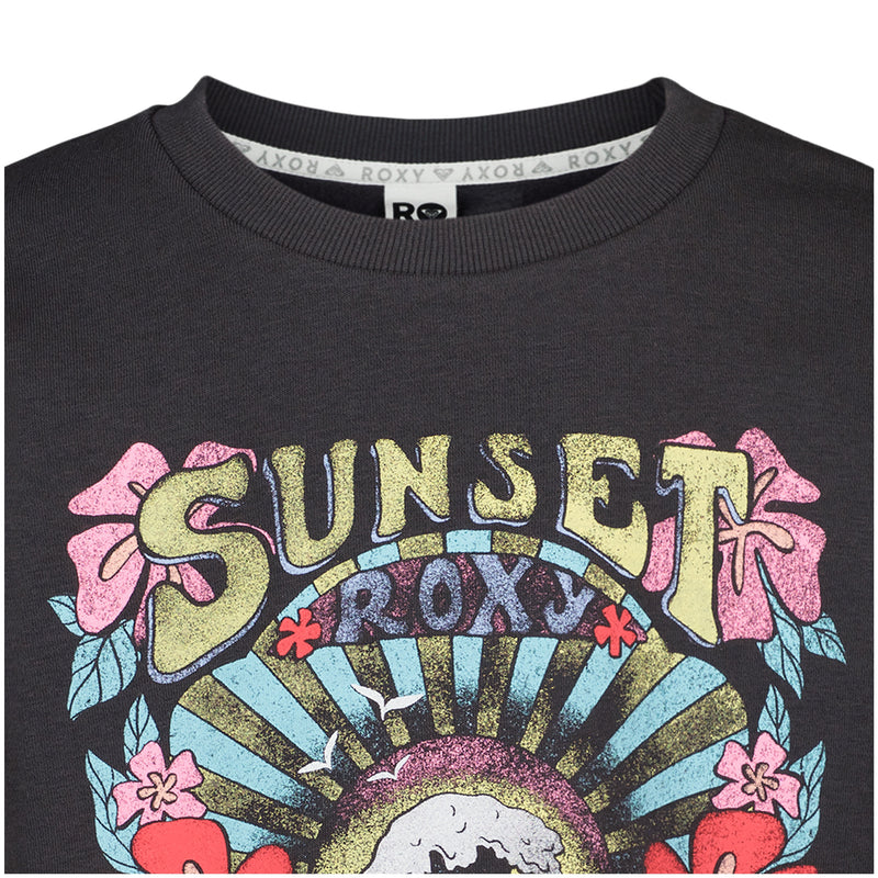 Close-up of the Girls' Sunny Crew by Roxy, an oversized dark crew with a colorful graphic featuring bold yellow "SUNSET" lettering, flowers, and a sunburst with "ROXY" below.