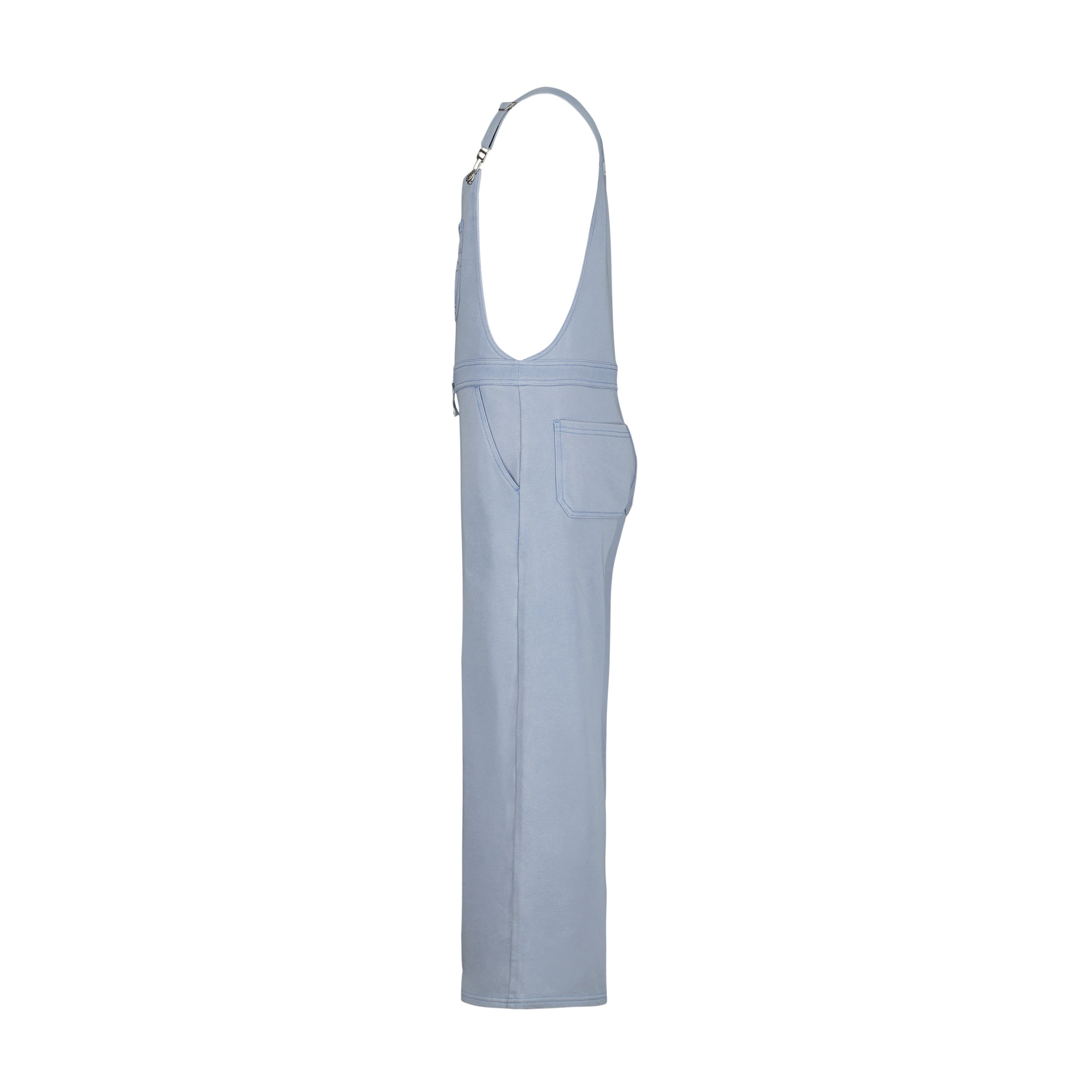 Girls' Coastline Overall by Roxy in light blue denim, shown side view with straight leg, side pocket, and adjustable metal-clip straps. Made of soft cotton-poly French terry. Set on a plain white background.