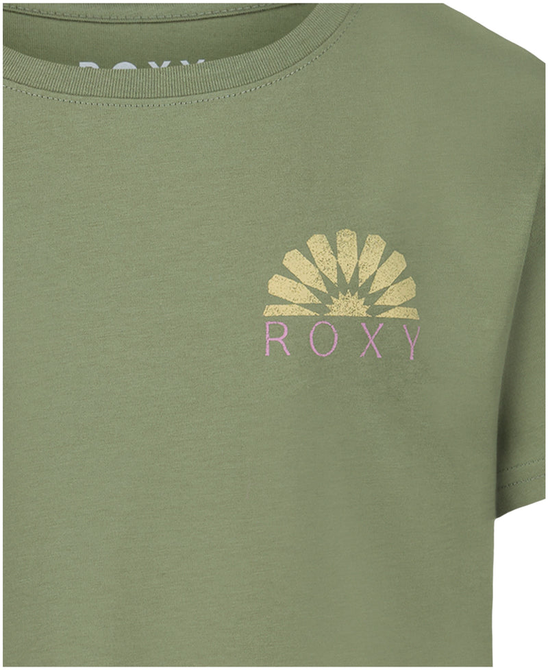 Close-up of the Girls' Sun Mosaic Tee by Roxy—a light olive green cotton jersey crew tee featuring an oversized fit, yellow sunburst graphic, and purple Roxy logo on the left chest. Only a portion of the shirt is visible.