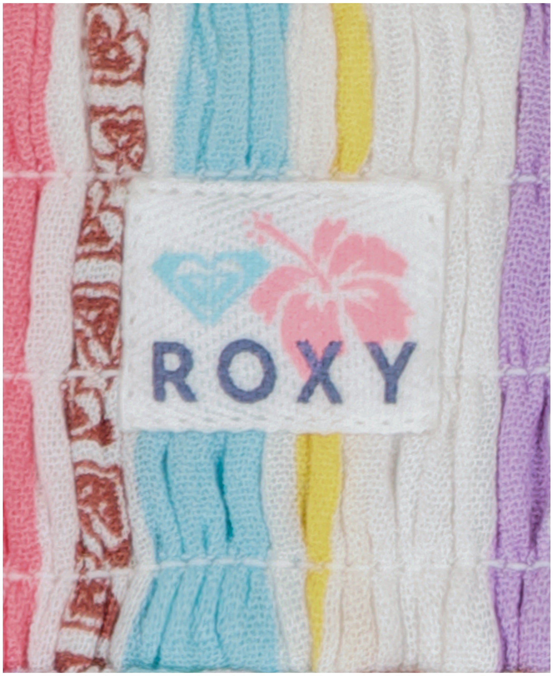 A close-up of the fabric label with "Roxy," a pink hibiscus, and a turquoise heart logo is sewn onto the pastel-striped Girls' Bali Stripe Pant by Roxy—showcasing its fun, colorful style.