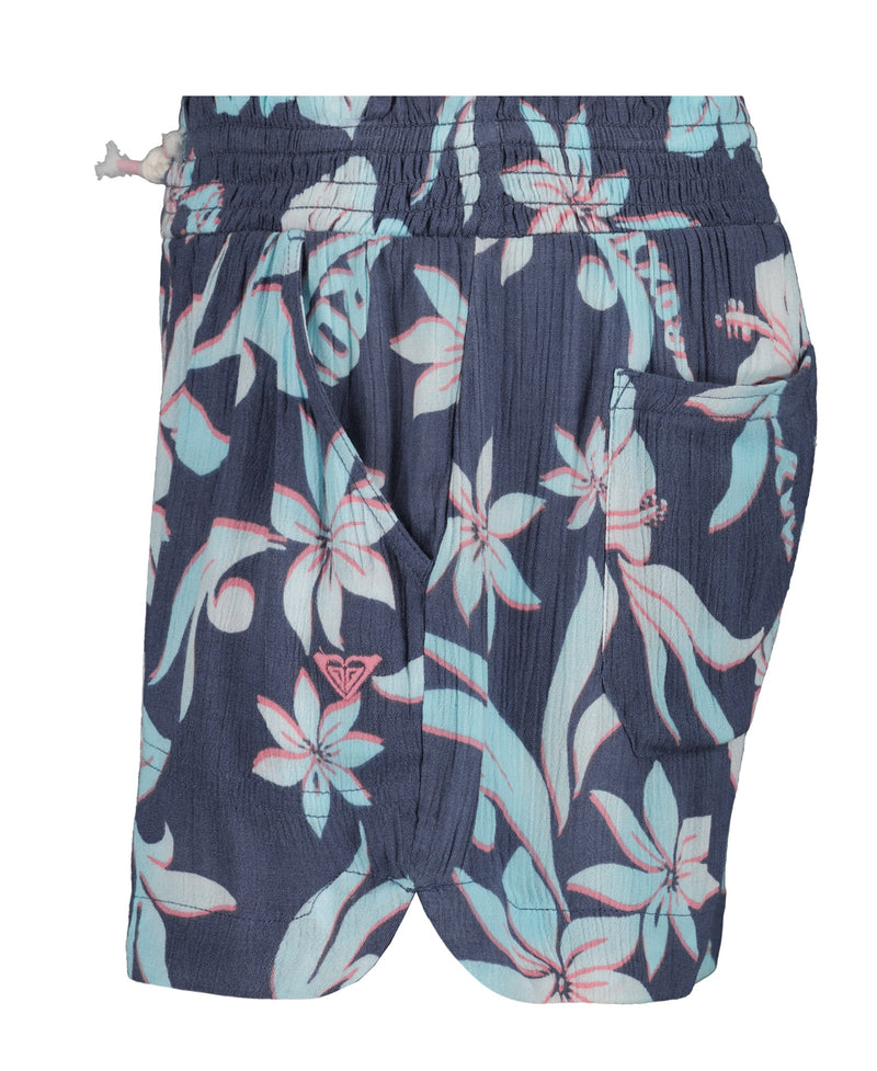 The Roxy Girls' Hula Soleil Short features a navy blue base with pink and light blue tropical florals, an elastic waistband, white drawstring, and side pocket—perfect for sunny beach days.