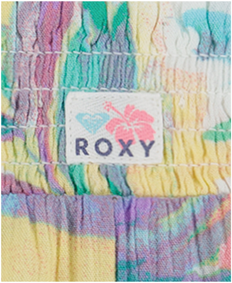 Close-up of a colorful, smocked fabric with a white label featuring a blue heart, pink hibiscus flower, and ROXY logo, capturing the pastel abstract palm print design of the Roxy Girls' Palm Sun Soleil Short.