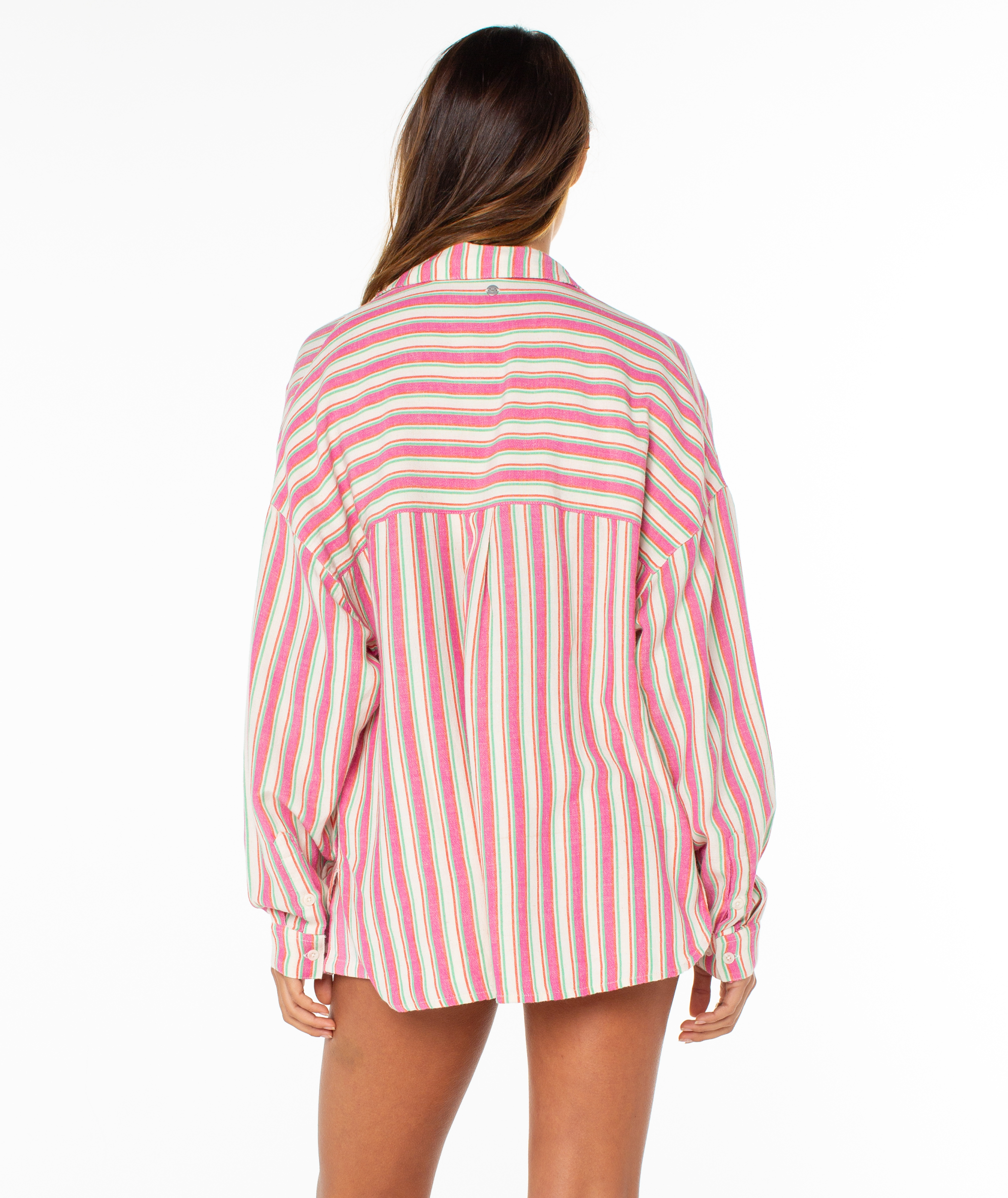 A person with long brown hair stands with their back to the camera, wearing the Roxy Lets Get Away Top—an oversized shirt featuring pink, red, and white vertical stripes—against a plain white background.