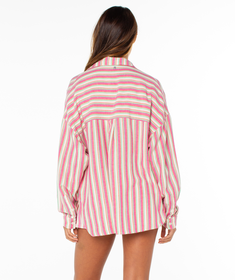 A person with long brown hair stands with their back to the camera, wearing the Roxy Lets Get Away Top—an oversized shirt featuring pink, red, and white vertical stripes—against a plain white background.