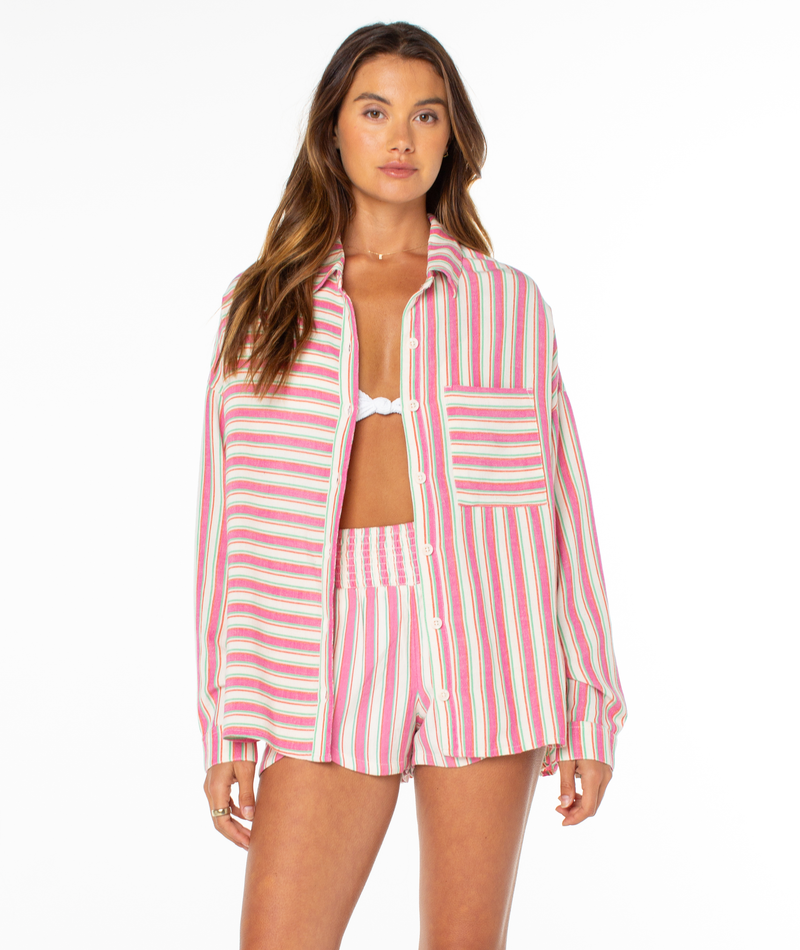 A woman wears the Roxy Lets Get Away Top—white bikini paired with a pink, green, yellow, and white striped shirt and shorts set—standing against a plain white background, her bold shirt adding a playful vibe.