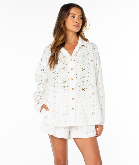 A woman models the Roxy Morning Time Top—a white, long-sleeve summer shirt—paired with matching eyelet shorts, standing with one hand in her pocket against a plain white background.