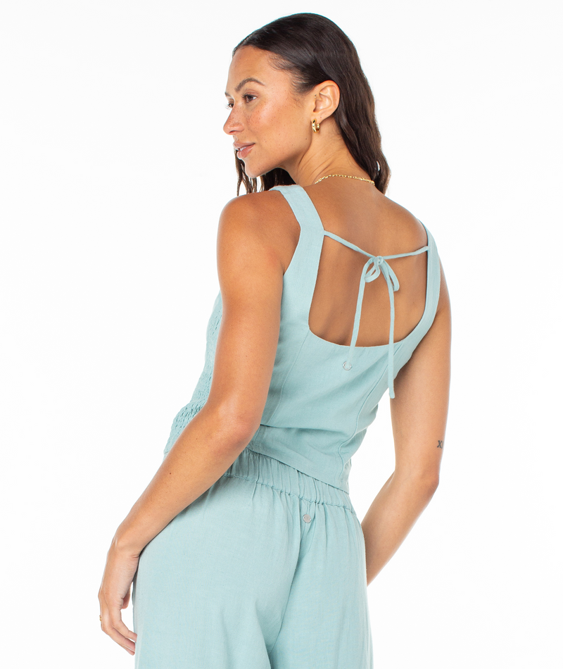 A woman wears the Roxy Maui Sessions Top, a light blue sleeveless piece with a square neckline and a thin tie across the open back.