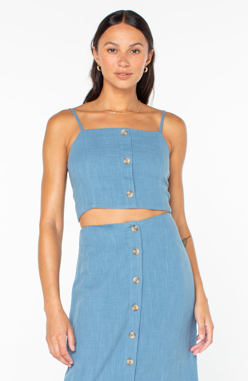 A woman wearing a blue, cropped, button-front Island Nomad Top by Roxy and a matching button-front skirt.