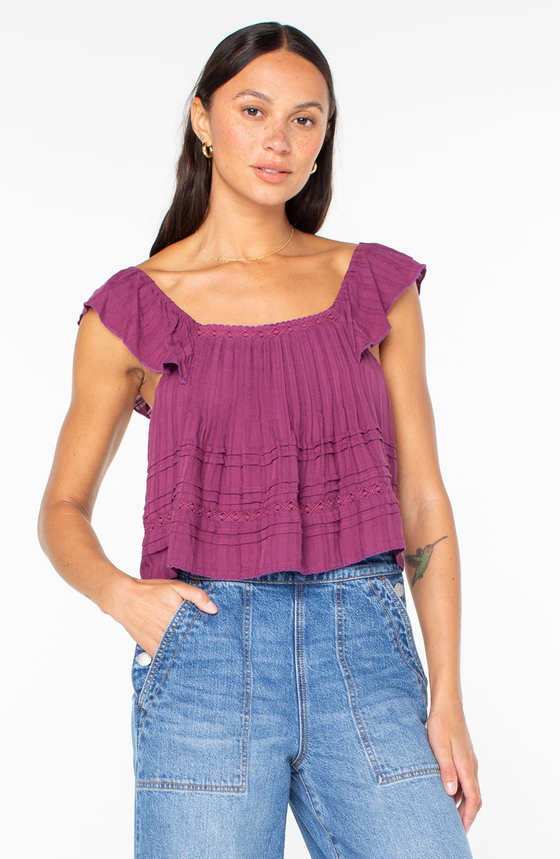 A woman wearing the Roxy Coastal Rays Top in amaranth solid, a sleeveless, deep magenta tiered design featuring ruffled sleeves and lace trim.