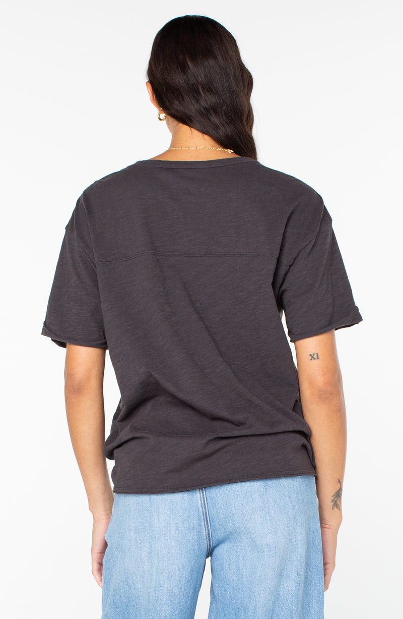 Back view of a person wearing a charcoal gray Sunset Sessions Tee and blue jeans.