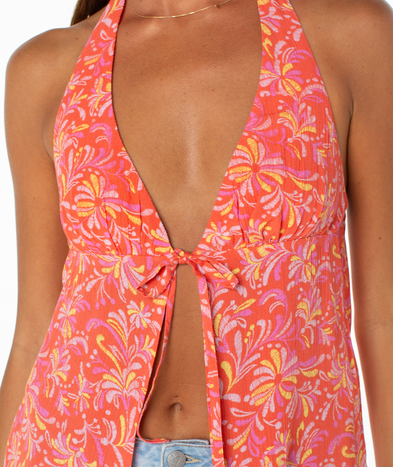 A woman wears the Roxy Fairweather Top—a sleeveless halter with a deep V neckline and pink, orange, and yellow floral pattern tied at the bust—paired with blue jeans. Only her upper torso is visible.