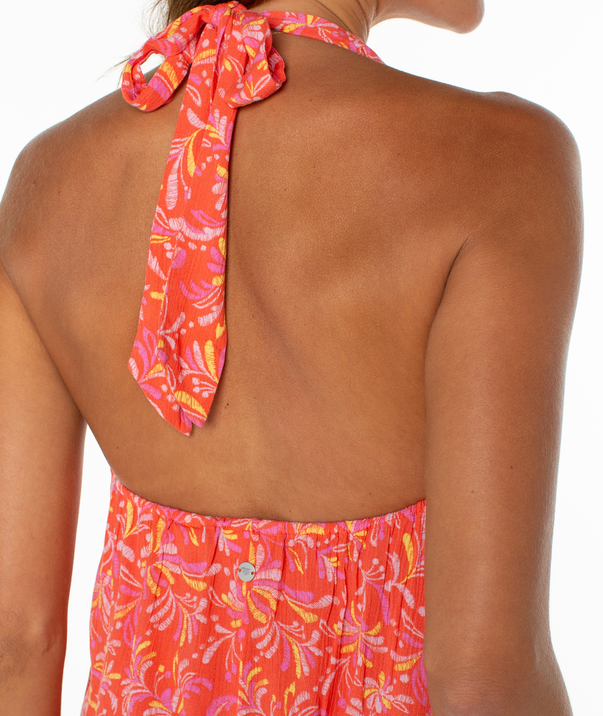 Woman’s back in the Roxy Fairweather Top, a bright orange floral halter with a neck tie, channeling retro beachwear style.