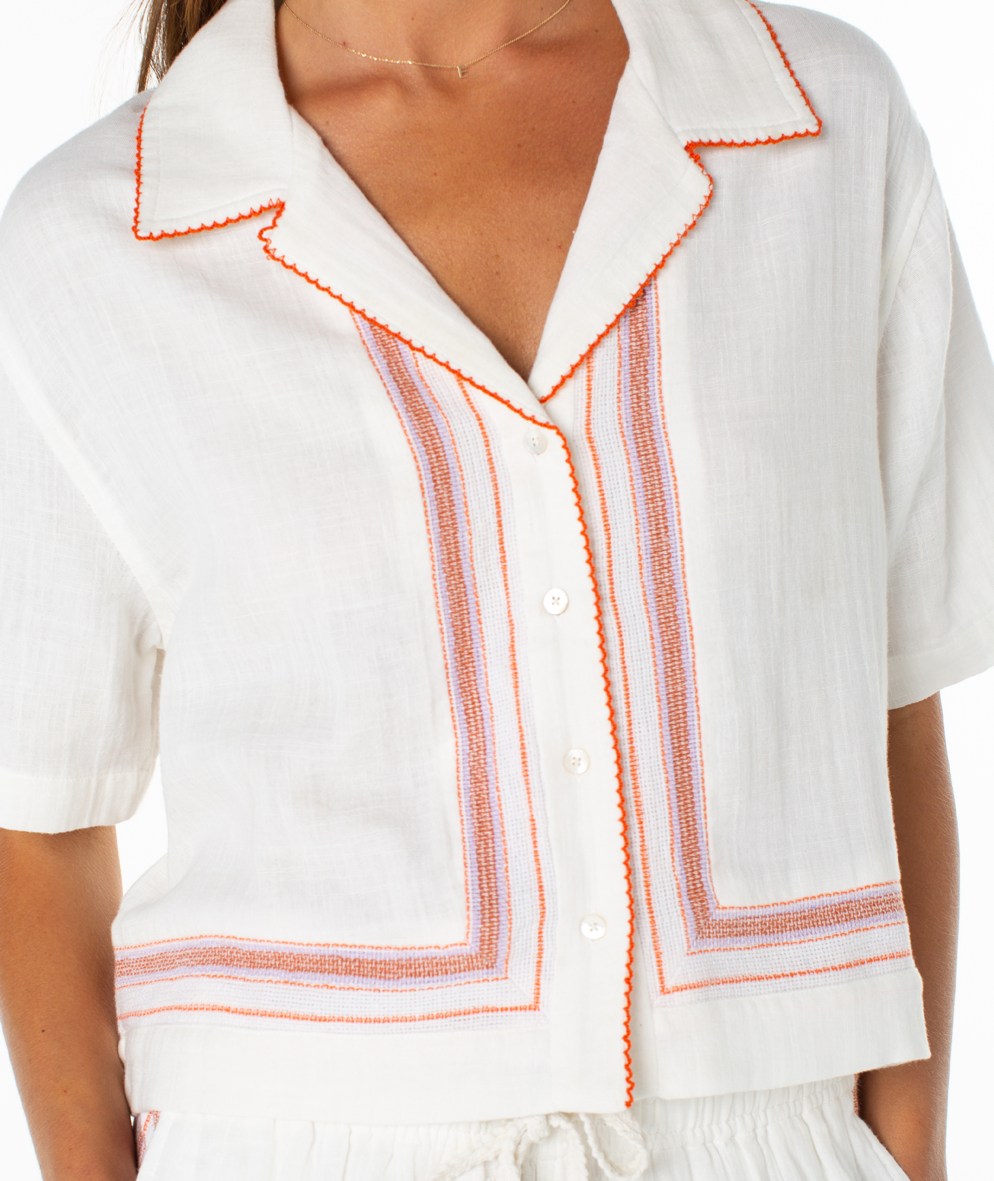 Close-up of a woman wearing the Roxy Fiesta Siesta Shirt, a white linen short-sleeve button-up with orange trim and vertical stripe embroidery—perfect for summery striped shirt vibes.