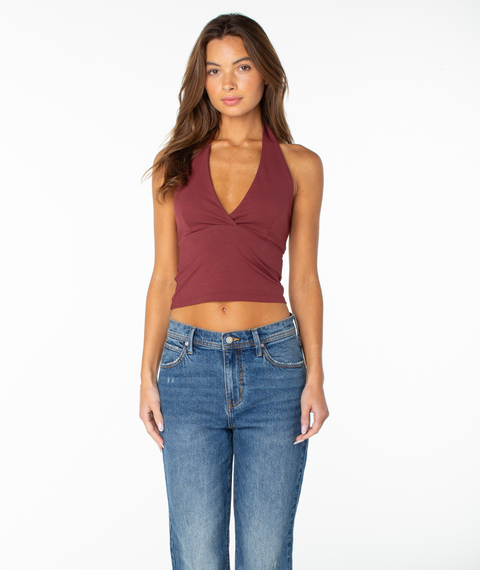A woman with long brown hair wears the Roxy South Shore Halter Tank in Port Solid—a sleeveless, cropped-fit top—paired with blue jeans, standing against a plain white background and looking at the camera with a neutral expression.
