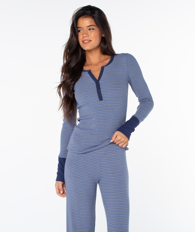 A woman with long brown hair wears the Hillside Long Sleeve Henley Top by Roxy, standing against a plain white background, looking to the side and smiling.