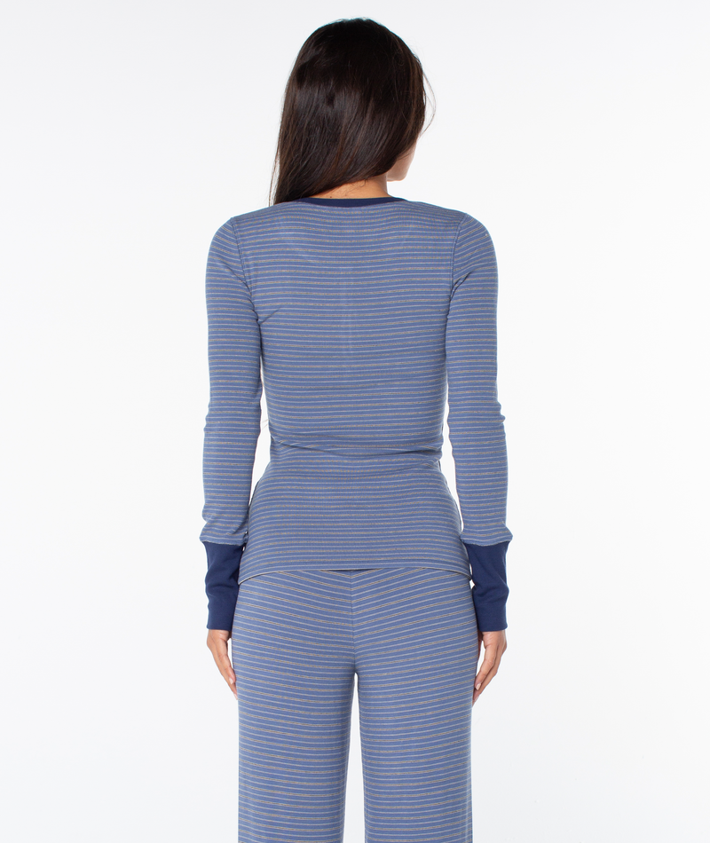 A woman with long brown hair wears the Roxy Hillside Long Sleeve Henley Top and matching pants, standing facing away against a white background.