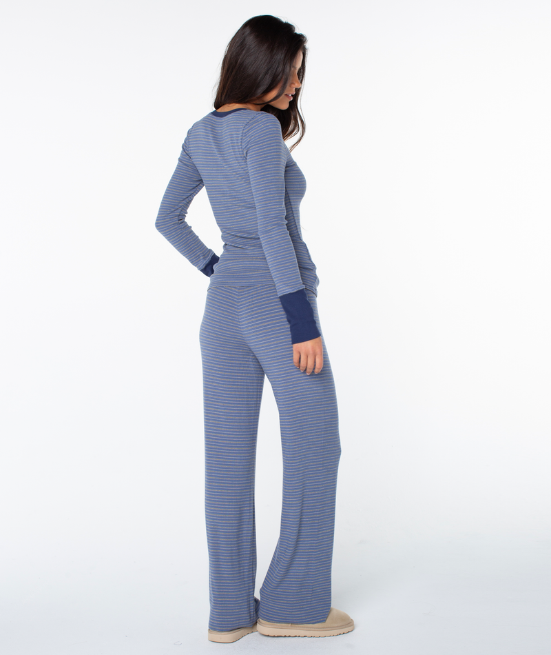 A woman stands facing away, wearing the Hillside Long Sleeve Henley Top by Roxy with wide-leg pants and slippers, set against a plain white background.