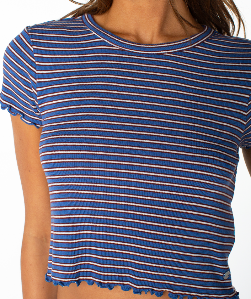 A person wearing the Roxy Poolside Crop Tee, a blue, short-sleeved, ribbed top featuring white and red horizontal stripes and ruffled edges—perfect for a stylish summer look.