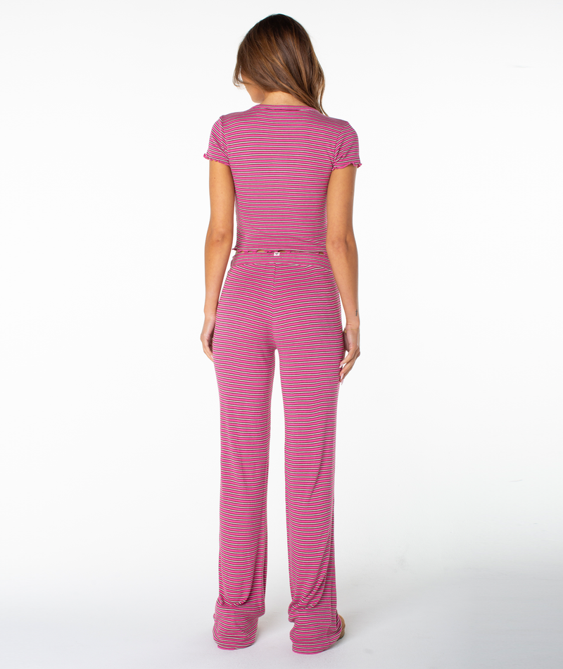 A woman faces away, wearing a fitted Poolside Crop Tee by Roxy in pink and gray stripes paired with matching high-waisted pants, her hair loose against a white background—perfect for summer style.
