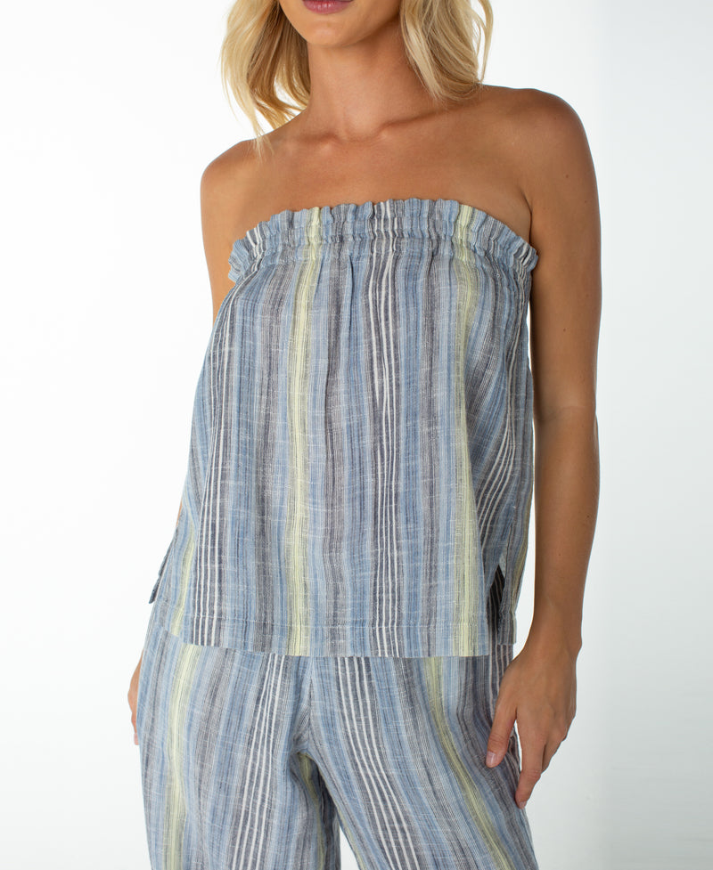 A woman stands against a plain background wearing the Roxy Offshore Top—a strapless, loose-fitting style—paired with matching pants featuring vertical blue, white, and yellow stripes, creating an ideal look for a tropical vacation.