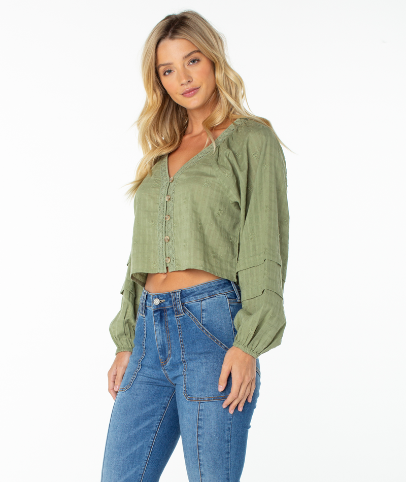 A woman with long blonde hair is wearing the Roxy Monterey Top, featuring oversized sleeves in green, paired with blue high-waisted jeans as she stands against a plain white background.