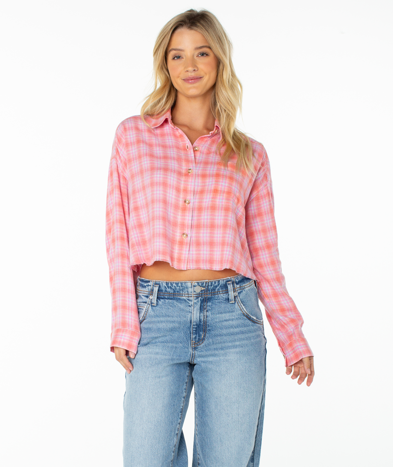 A woman with long blonde hair smiles while standing against a plain white background, wearing the Roxy Rockford Top in Camellia Sunburst Plaid and light blue jeans.