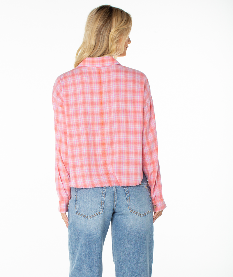 A woman with long blonde hair is seen from behind, wearing the Roxy Rockford Top—a pink and white plaid flannel long-sleeve shirt—paired with light blue jeans against a plain white background.