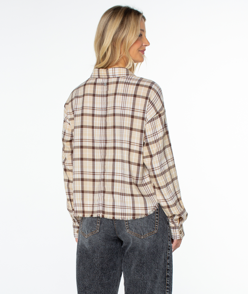 A woman with blonde hair models the Roxy Rockford Top—an oversized beige and brown plaid shirt—paired with dark jeans, standing with her back to the camera against a plain white background.