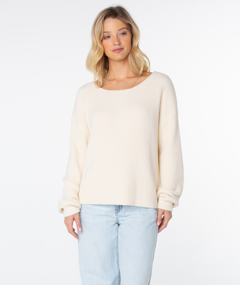 A woman with blonde hair wears the Roxy Bombay 2 Sweater in cream with light blue jeans, standing against a plain white background.