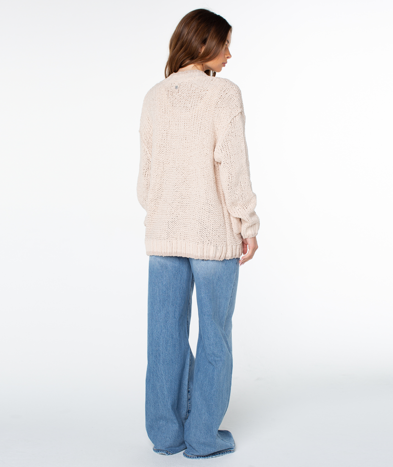 A person seen from behind wearing an oversized, cream-colored Roxy Cozy Cruiser cardigan and wide-leg blue jeans.
