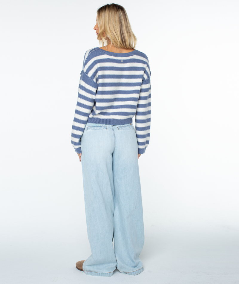 A person stands facing away in a blue and white Swell Season Stripe Sweater by Roxy and light blue wide-leg jeans, creating a relaxed silhouette against a plain white background.