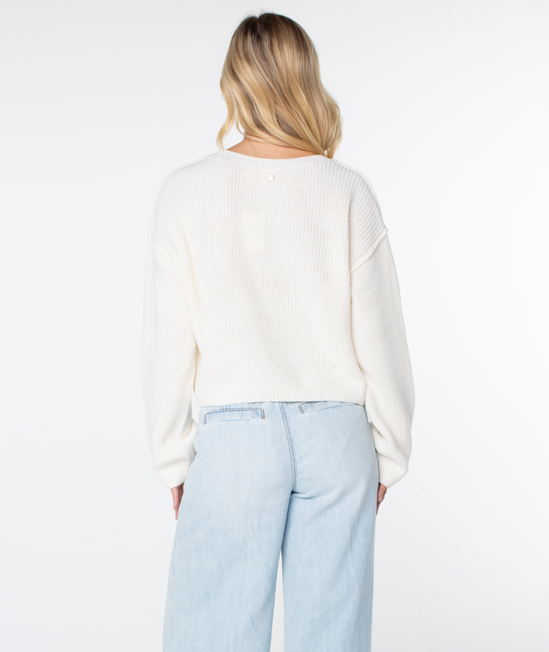 A person with long blonde hair wears the Roxy Swell Season Sweater and light blue jeans, facing away from the camera against a plain white background.