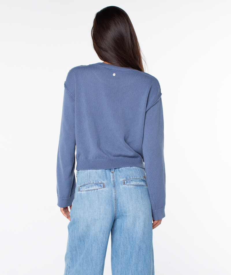 A person with long dark hair, seen from the back, wears the Swell Season Sweater by Roxy and light blue jeans, standing against a plain white background.