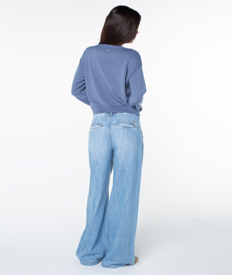 Woman standing with her back to the camera, wearing the Roxy Swell Season Sweater and wide-leg light blue jeans against a plain white background.