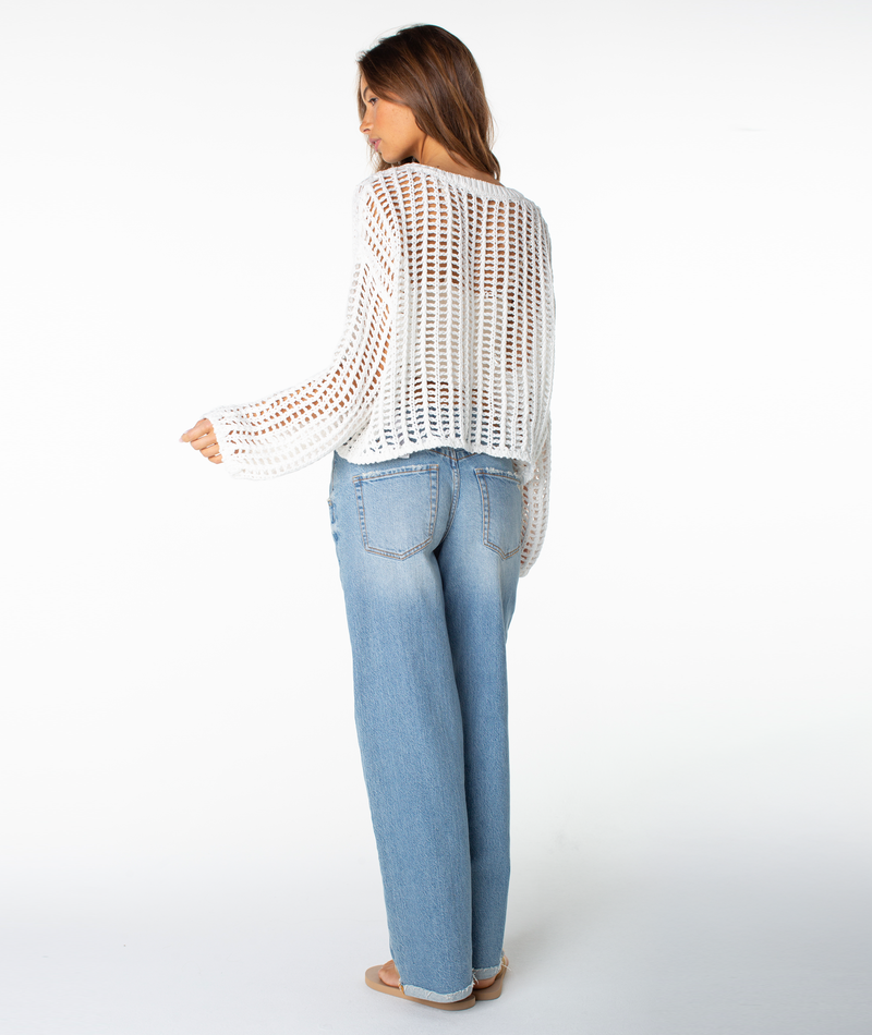 Woman wearing the Roxy Lost At Sea Long Sleeve Top over a tan tank and light blue distressed jeans with tan sandals—this White crochet top is an easy-to-style statement piece for any casual day.