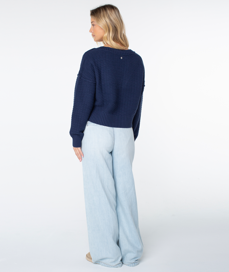 A person seen from the back wearing a cozy navy blue textured Study Hall Sweater by Roxy and light-wash wide-leg jeans.