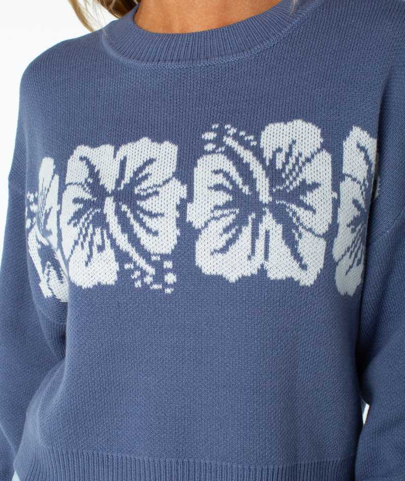 A person wears the Roxy Hibiscus Harmony Sweater, featuring a white hibiscus pattern on blue cotton blend—perfect for breezy beach nights.