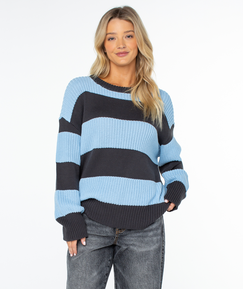 A woman wearing a cozy, oversized chunky knit Roxy West Side Sweater featuring black and light blue horizontal stripes.