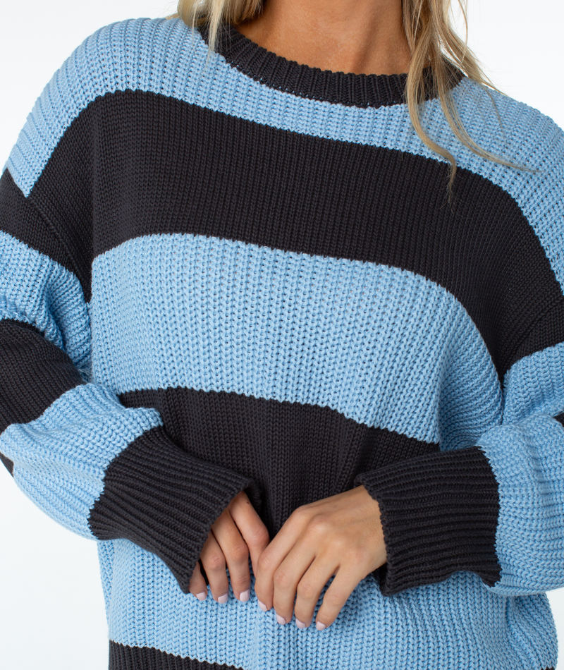 A person wearing a Roxy West Side Sweater, an oversized chunky knit crewneck featuring thick horizontal stripes in light blue and black.
