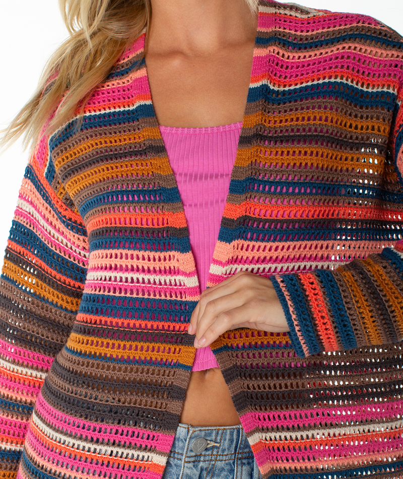 A person wearing a pink ribbed top, the Roxy Sea Wind Cardigan—a colorful striped cotton blend—and light blue jeans. Only their lower face and torso are visible.