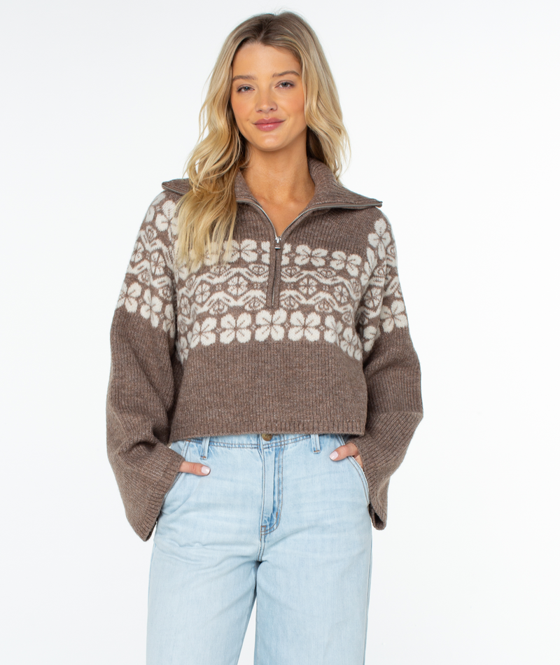 Woman wearing a relaxed fit, brown cropped quarter-zip Roxy Cedar Grove Sweater with a white floral pattern across the chest and shoulders.