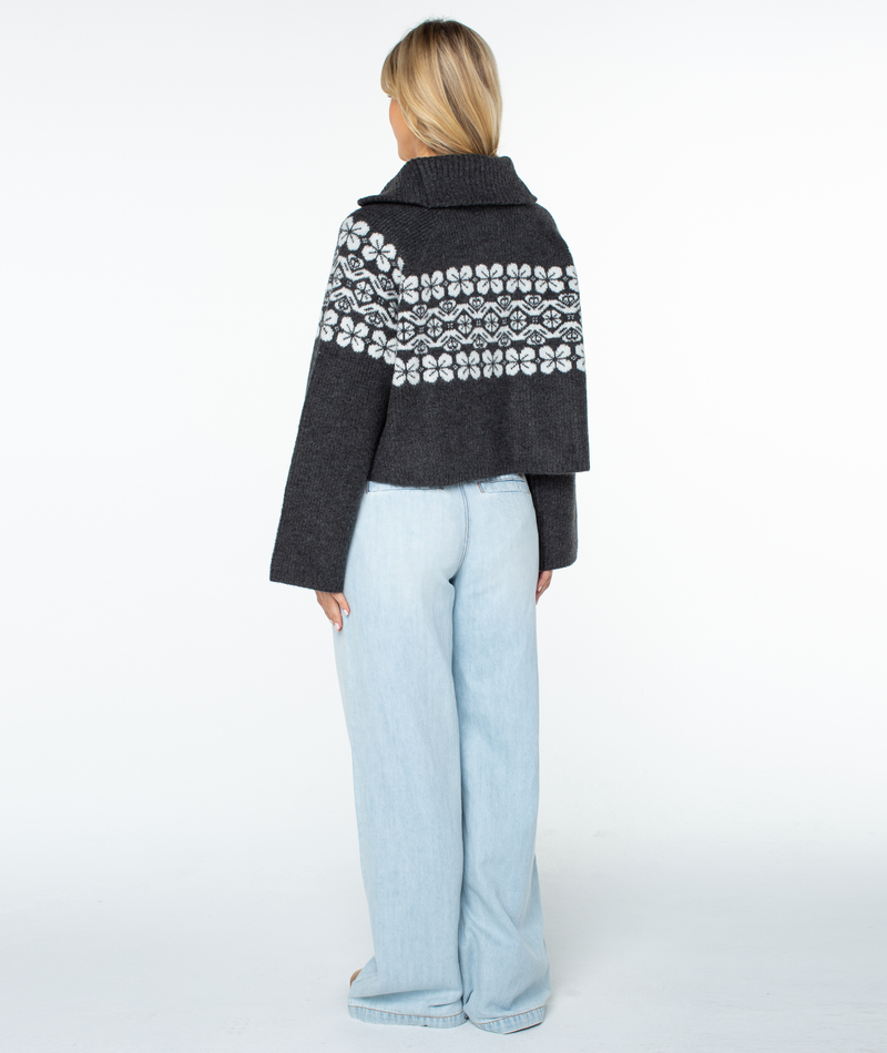 Back view of a person wearing a Roxy Cedar Grove Sweater, a charcoal gray, cropped quarter-zip with a white floral pattern, paired with light-wash wide-leg jeans for a relaxed fit.