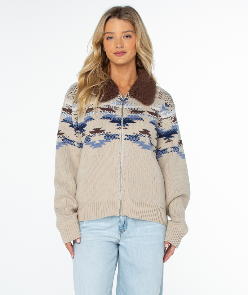 The Roxy Wildwood Sweater is a beige, full-zip knit cold-weather staple featuring a brown collar and a statement blue and grey geometric pattern across the chest and shoulders.