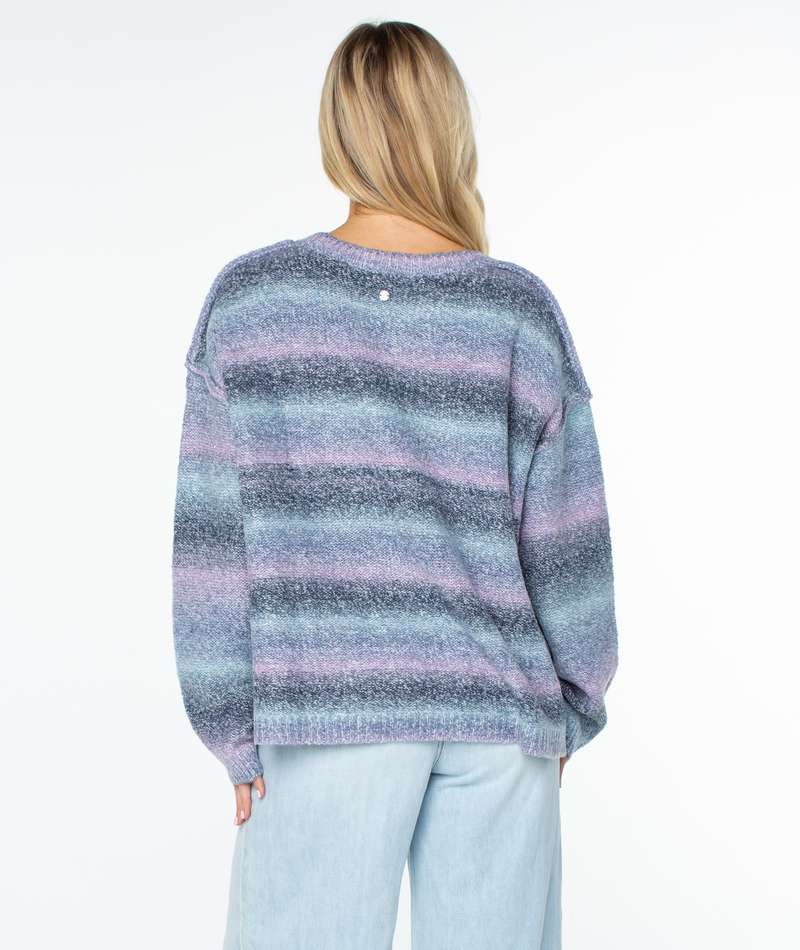 A person seen from behind wears the Roxy Cold Front Sweater, a slouchy, relaxed-fit crew-neck with horizontal stripes in shades of blue, purple, and gray.