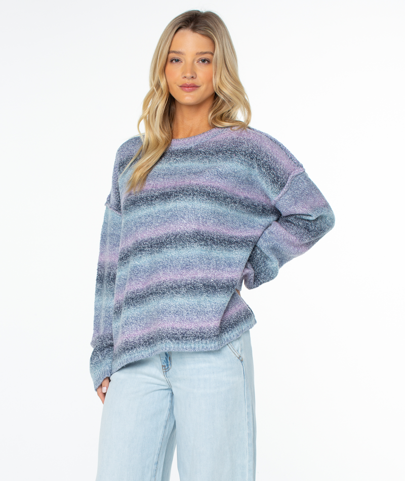 A person wearing a slouchy, long-sleeved, crewneck Roxy Cold Front Sweater with horizontal stripes in shades of blue and purple.