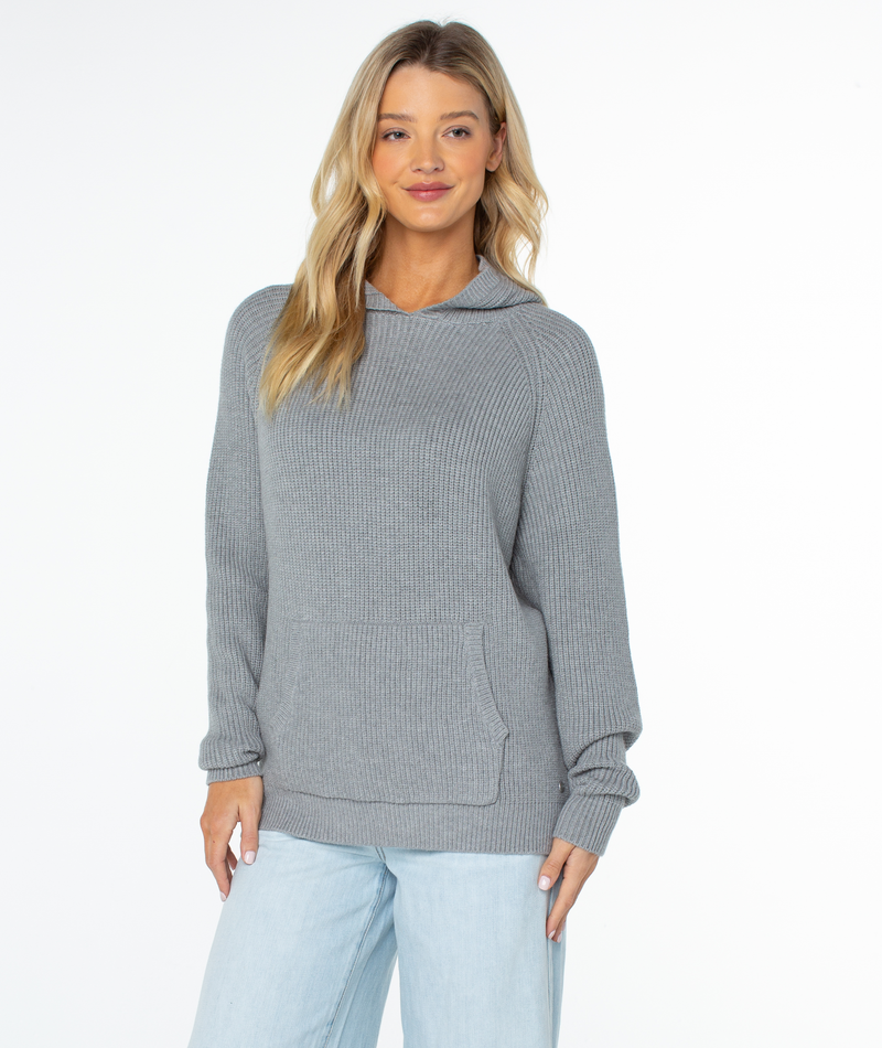 A person wearing a cozy Roxy Cozy Town Sweater with a front kangaroo pocket and light-wash jeans.