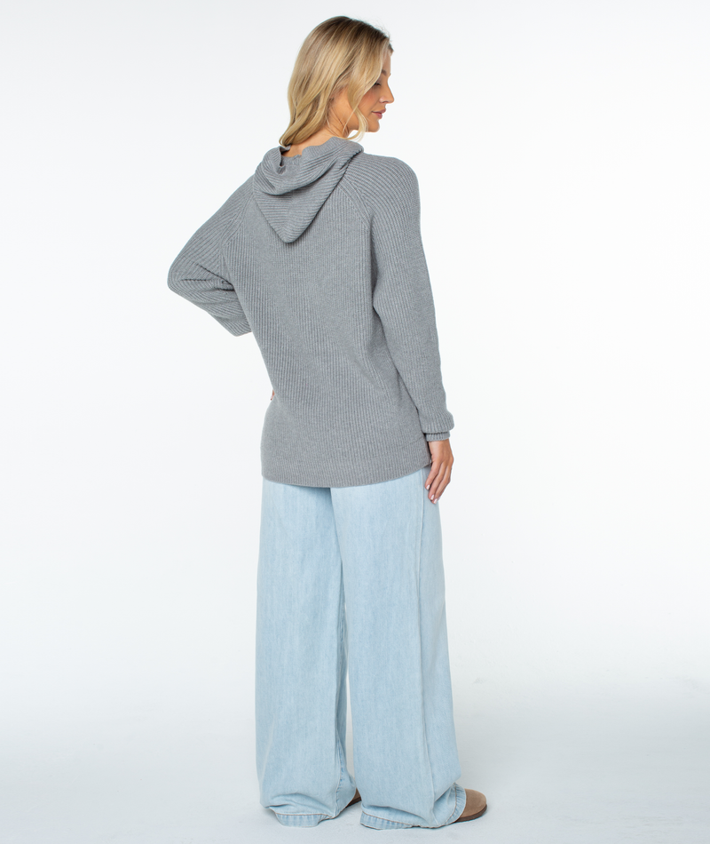 A woman seen from behind wears a grey ribbed-knit Roxy Cozy Town Sweater hoodie and light-wash wide-leg jeans.